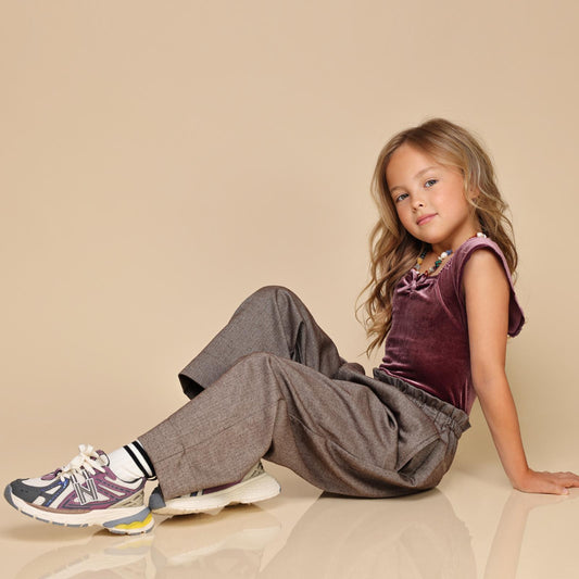 Zittend meisje in stijlvol pakje met witte LilPataz kindersneakers met paarse details – zijaanzicht