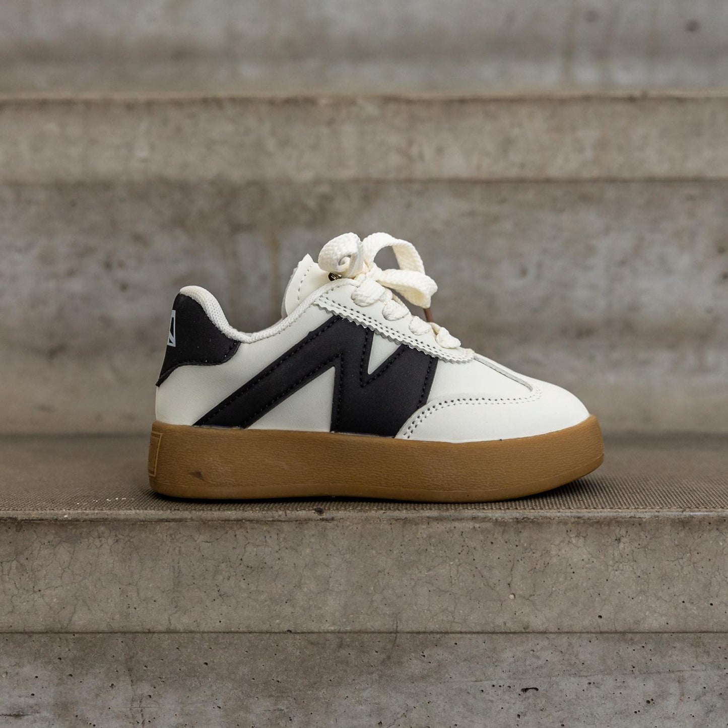 Zijaanzicht van de Sunnyz Black kindersneaker – stijlvolle witte sneaker met zwart logo en stevige zool